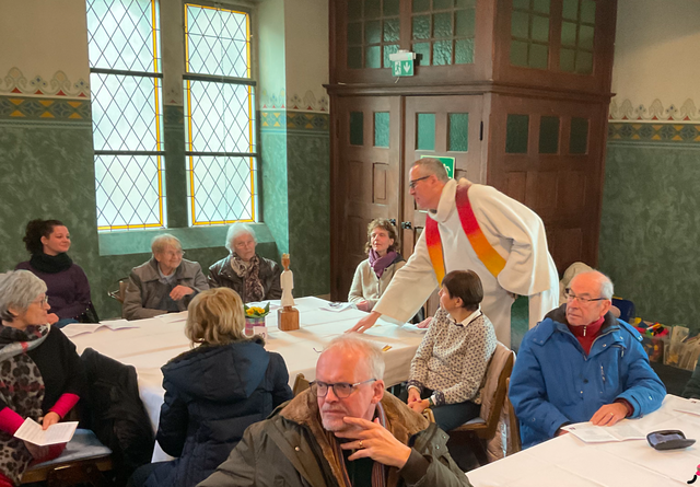Andreas Sturm, Pfarrer der Alt-Katholischen Gemeinden Singen und Saulbach, überbringt eine weitere Königsskulptur des Bonner Diakons und Holzbildhauers Ralf Knoblauch an Tisch Nummer 20 im Kirchensaal der achten Singener Vesperkirche. | Foto: Bernhard Grunewald